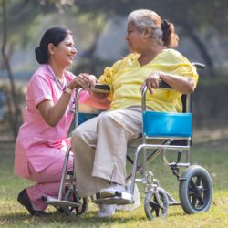 Indian caregiver nurse taking care of senior female patient in a wheelchair at park.